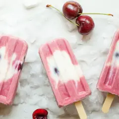 Ghiaccioli fatti in casa con ciliegie e yogurt, su un letto di ghiaccio tritato. Freschi e invitanti, perfetti per l'estate.