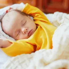 Dolce neonato piange nel sonno, avvolto in una coperta calda. Le sue braccia sono sollevate, come in un sogno agitato.