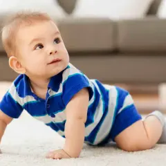 Un adorabile neonato di 8 mesi, con indosso una maglietta a righe blu e bianche, gattona curioso su un tappeto chiaro, esplorando il mondo.