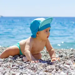 Un bimbo con cappellino blu esplora la spiaggia, curioso del mare. Un'immagine di neonati al mare che cattura la meraviglia.