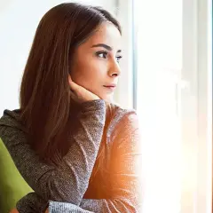 Donna pensierosa guarda fuori dalla finestra, preoccupata per un ciclo in ritardo e come farlo venire.