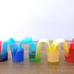 Colorati esperimenti per bambini: strisce di carta assorbono liquidi colorati in bicchieri trasparenti, creando un arcobaleno liquido.