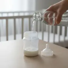 Preparazione del biberon con latte vaccino per bambini. Acqua versata da una bottiglia in un biberon con latte.