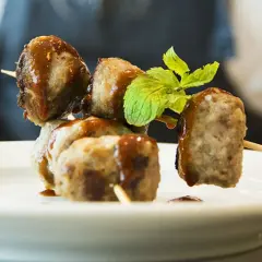 Spiedini di polpette di fagioli, condite con salsa e guarnite con menta fresca, su un piatto bianco.