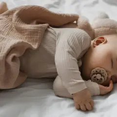 Un neonato dorme sereno con un ciuccio, avvolto in una coperta color pesca. Un'immagine che ispira su come far addormentare un neonato.