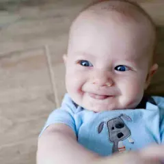 Sorriso contagioso di un neonato con occhi azzurri brillanti, un vero test colore occhi neonato. Indossa una tutina azzurra con un cagnolino.