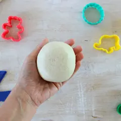 Mano che tiene una palla di pasta di sale, pronta per creare forme con stampini colorati e attrezzi. Ricetta facile per divertirsi.