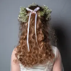Capelli ricci con coroncina di fiori e nastri, perfetti per trecce acconciature comunione.