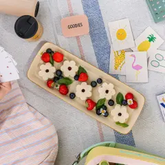 Picnic per bambini con panini a forma di fiore, fragole, mirtilli e carte da gioco colorate.