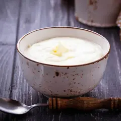 Una ciotola di semolino dosi per 1 persona con latte, guarnita con un pezzetto di burro. Un cucchiaio di legno è appoggiato accanto.