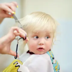 Bambino biondo con occhi azzurri riceve il suo primo taglio capelli, un momento speciale immortalato con cura.