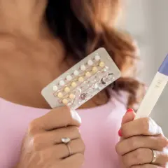 Donna tiene in mano un blister di pillole anticoncezionali e un test di gravidanza positivo. Si interroga su come rimanere incinta con la pillola e sui sintomi.