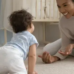 Un neonato di 9 mesi gattona verso la madre sorridente, in una stanza luminosa.