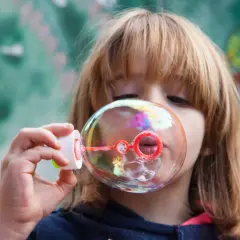 Bambina soffia bolle di sapone iridescenti. Una ricetta veloce per un momento di gioia.