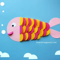 Pesciolino colorato creato con lavoretti per bambini in estate. Bollicine e onde di carta completano la scena marina.