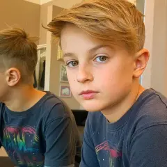 Ragazzo con taglio capelli bambino 11 anni, capelli biondi sfilati e ciuffo. Riflesso nello specchio.