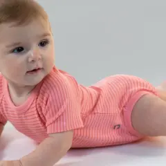 Un adorabile neonato di 7 mesi, sdraiato a pancia in giù, indossa un body a righe corallo.