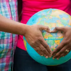 Mani a forma di cuore circondano un globo, simbolo del desiderio di adottare un bambino e accoglierlo nel mondo.