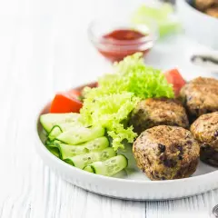 Polpette lenticchie e patate dorate, servite con insalata fresca, pomodoro e cetrioli a spirale. Un piatto gustoso e salutare.