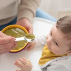Bambino curioso assaggia la sua prima pappa svezzamento, con un cucchiaino pieno di verdure.