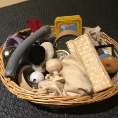 Un cestino dei tesori pieno di oggetti curiosi: un tubo grigio, una pallina da golf, un piccolo specchio, una scatola gialla e altri elementi da esplorare.