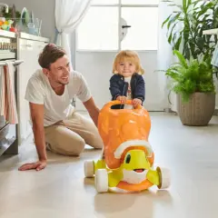 Un papà sorridente incoraggia i primi passi del suo bambino su un cavalcabile a forma di tartaruga in cucina.