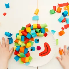 Bambini creano un clown con carta colorata, un'idea per giochi di carnevale. Ritagli di carta colorata e forbici.