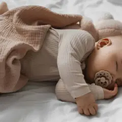Dolce neonato di 3 mesi dorme sereno, avvolto in una copertina color pesca, con un ciuccio in bocca.