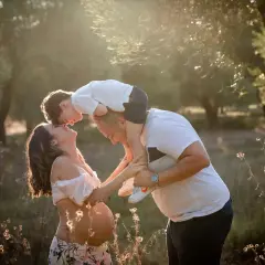 Una bellissima giornata della famiglia, con un bimbo sulle spalle del papà che bacia la mamma in dolce attesa, immersi nella luce dorata del tramonto.
