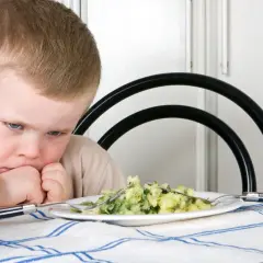 Bambino con espressione di disgusto davanti a un piatto di purè e verdure. Il suo volto mostra un riflesso di estrusione, come se volesse fuggire da quel cibo.