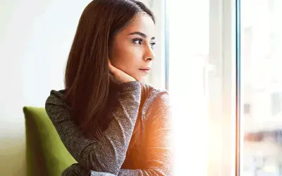 Donna pensierosa guarda fuori dalla finestra, preoccupata per un ciclo in ritardo e come farlo venire.