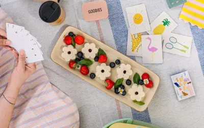 Picnic per bambini con panini a forma di fiore, fragole, mirtilli e carte da gioco colorate.