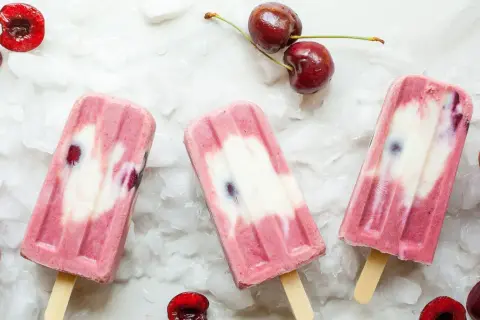 Ghiaccioli fatti in casa con ciliegie e yogurt, su un letto di ghiaccio tritato. Freschi e invitanti, perfetti per l'estate.