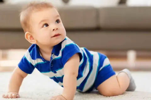 Un adorabile neonato di 8 mesi, con indosso una maglietta a righe blu e bianche, gattona curioso su un tappeto chiaro, esplorando il mondo.