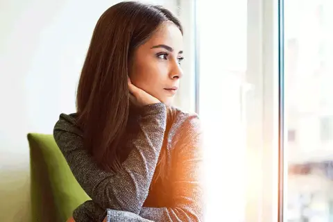Donna pensierosa guarda fuori dalla finestra, preoccupata per un ciclo in ritardo e come farlo venire.