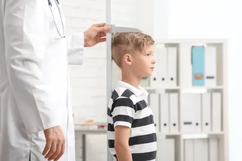 Un bambino viene misurato da un medico. La domanda "quanto sarà alto mio figlio" aleggia nell'aria mentre si attende il risultato.