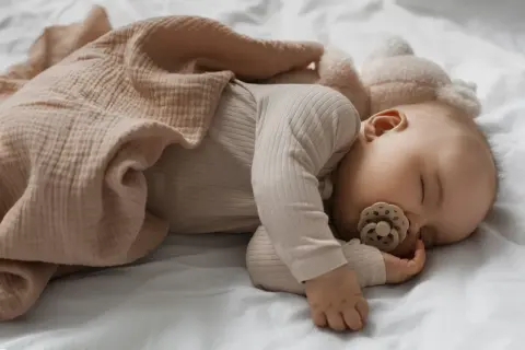 Un neonato dorme sereno con un ciuccio, avvolto in una coperta color pesca. Un'immagine che ispira su come far addormentare un neonato.