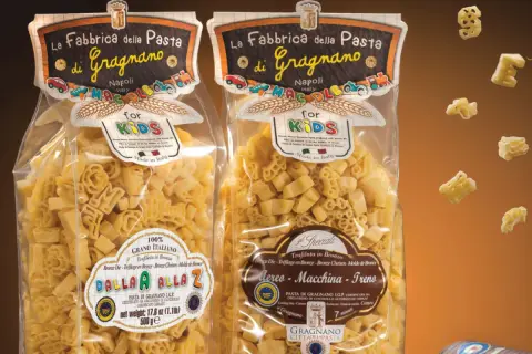 Due confezioni di pasta per bambini, una con lettere e l'altra con aerei, macchine e treni, prodotte a Gragnano.