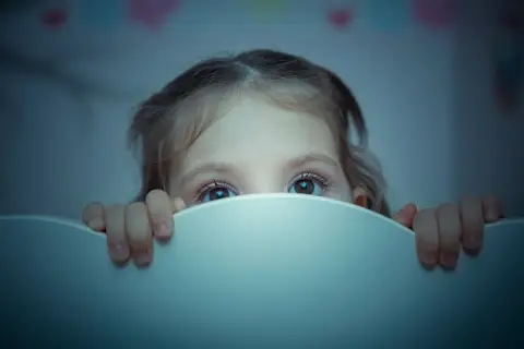 Occhi spaventati di un bambino di 2 anni che si sveglia piangendo disperato nel buio.