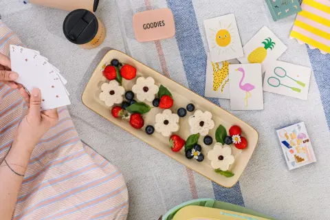 Picnic per bambini con panini a forma di fiore, fragole, mirtilli e carte da gioco colorate.