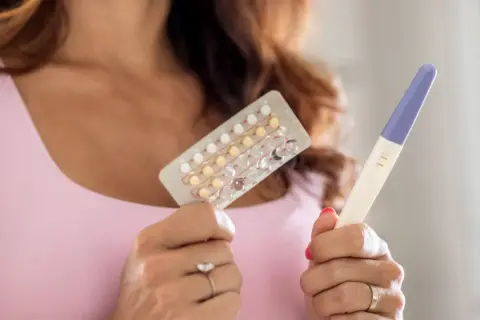 Donna tiene in mano un blister di pillole anticoncezionali e un test di gravidanza positivo. Si interroga su come rimanere incinta con la pillola e sui sintomi.