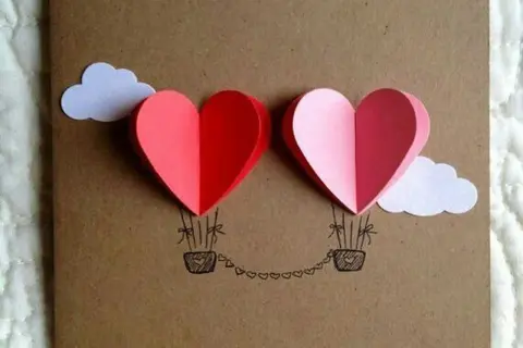 Lavoretto festa della mamma infanzia: due mongolfiere a forma di cuore rosse e rosa, con nuvole bianche e cesti disegnati.