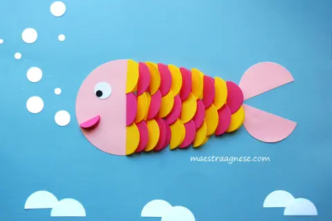 Pesciolino colorato creato con lavoretti per bambini in estate. Bollicine e onde di carta completano la scena marina.
