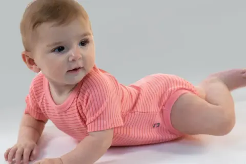 Un adorabile neonato di 7 mesi, sdraiato a pancia in giù, indossa un body a righe corallo.