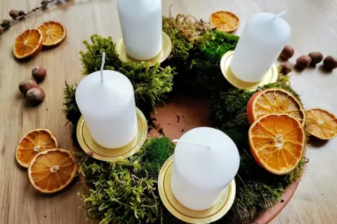 Corona dell'avvento fai da te con muschio, candele bianche, fette d'arancia essiccata e nocciole.