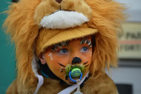 Bambino con trucco carnevale facile da leone, con ciuccio e cappello giallo.