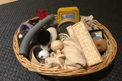Un cestino dei tesori pieno di oggetti curiosi: un tubo grigio, una pallina da golf, un piccolo specchio, una scatola gialla e altri elementi da esplorare.