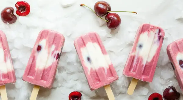 Ghiaccioli fatti in casa con ciliegie e yogurt, su un letto di ghiaccio tritato. Freschi e invitanti, perfetti per l'estate.