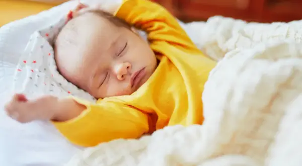 Dolce neonato piange nel sonno, avvolto in una coperta calda. Le sue braccia sono sollevate, come in un sogno agitato.