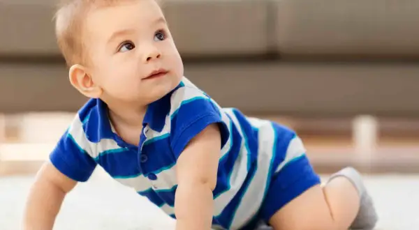 Un adorabile neonato di 8 mesi, con indosso una maglietta a righe blu e bianche, gattona curioso su un tappeto chiaro, esplorando il mondo.